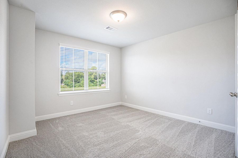 This room features neutral walls and carpet, a large window providing natural light, and a simple ceiling light fixture, offering a bright and versatile space.