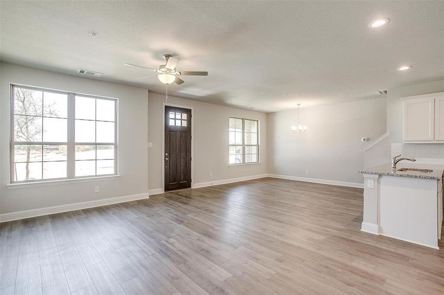 Unfurnished living room with ceiling fan, light wood-style flooring, and a chandelier