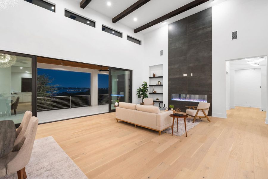 A spacious living area with soaring ceilings and light wood floors opens to a large balcony overlooking city lights.