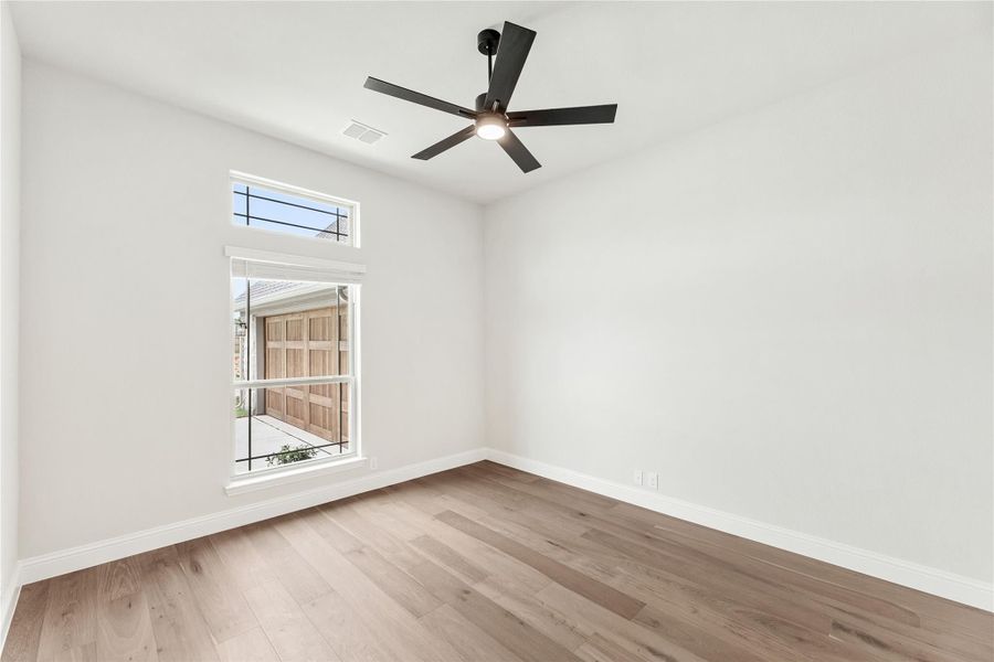 Empty room with light wood floors, white walls, black ceiling fan, and a window with exterior view