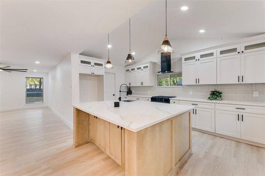 Kitchen featuring high end stove, lofted ceiling, an island with sink, light stone countertops, and white cabinets