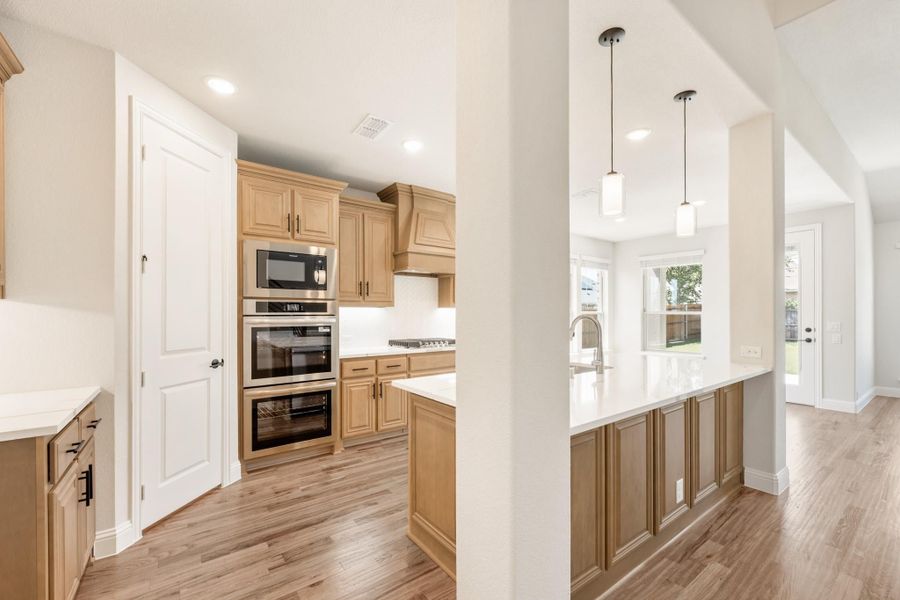 Kitchen with light wood cabinets, stainless steel double ovens, white island, and pendant lights over breakfast bar Kitchen with light wood cabinets, stainless steel double ovens, white island, and pendant lights over breakfast bar