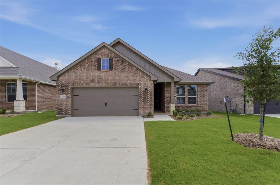 Brick facade residence featuring an attached garage, a paved driveway, and established landscaping