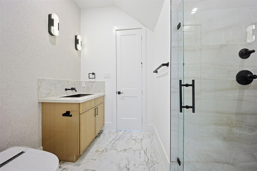 The bathroom offers a light wood vanity with a marble-patterned countertop, black fixtures, and contemporary wall sconces.