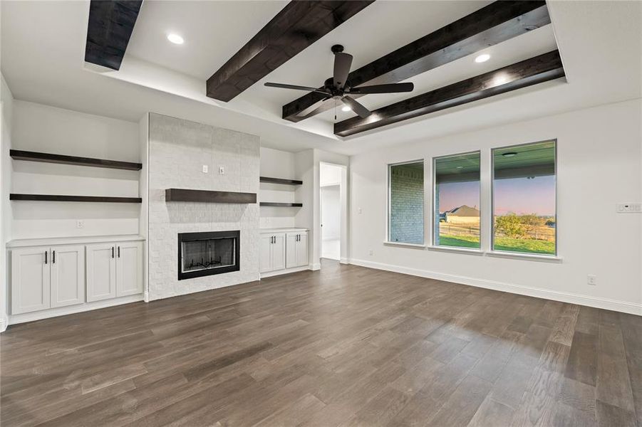 Unfurnished living room featuring beam ceiling, dark wood-style flooring, a fireplace, and ceiling fan