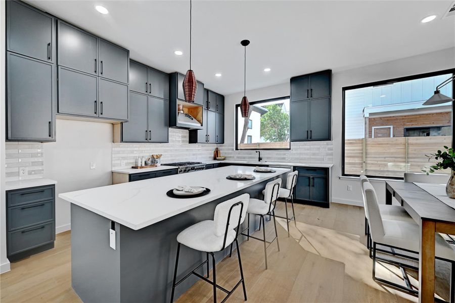 Kitchen with a breakfast bar area, hanging light fixtures, a kitchen island, gray cabinets, and tasteful backsplash