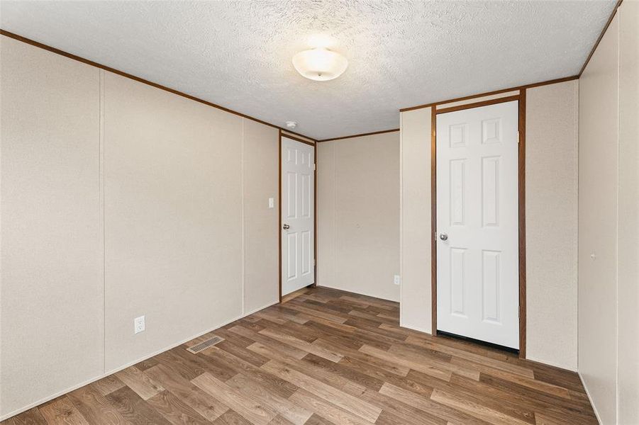 Unfurnished bedroom featuring wood finished floors, a textured ceiling, crown molding, and a decorative wall