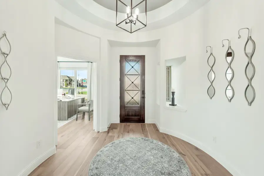 Foyer with round tray ceiling, dark wood front door with glass panels, chandelier, and light hardwood floors