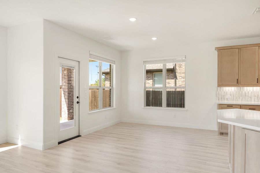 Bright dining area with light wood floors, back door, and adjacent kitchen with wood cabinets