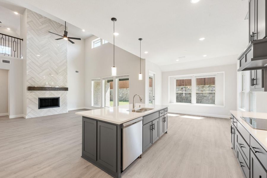 Open-concept kitchen with gray island, pendant lights, and tile fireplace accent wall in adjoining living area