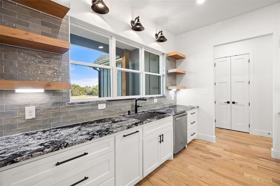 Kitchen with sink, tasteful backsplash, light hardwood / wood-style flooring, stainless steel dishwasher, and white cabinets