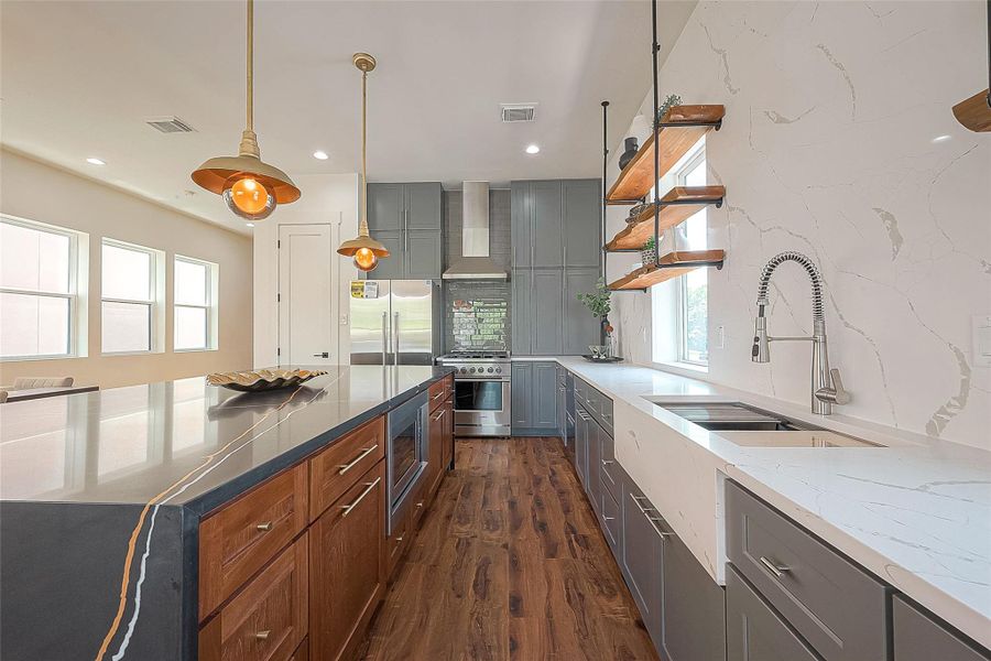 This modern kitchen features dark wood flooring, sleek gray cabinetry, and white countertops with a marble-like finish. It includes stainless steel appliances, floating wooden shelves, and stylish pendant lights. The space is bright with natural light from multiple windows. This modern kitchen features dark wood flooring, sleek gray cabinetry, and white countertops with a marble-like finish. It includes stainless steel appliances, floating wooden shelves, and stylish pendant lights. The space is bright with natural light from multiple windows.