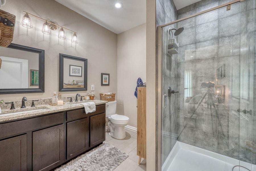 Contemporary bathroom featuring a dual vanity with granite-style countertops, dark wood-finish cabinetry, and framed mirrors