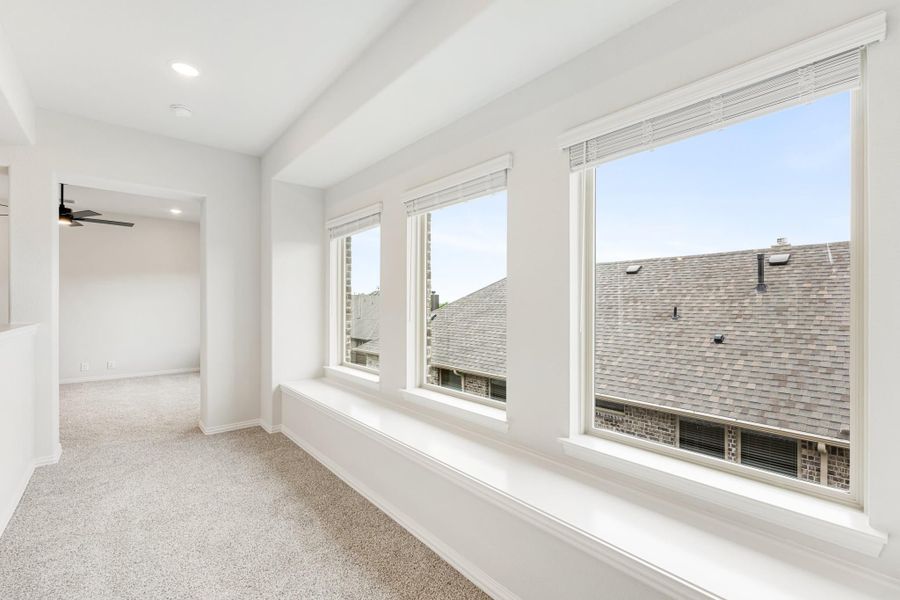 Bright empty bedroom with large windows, window seat, carpet, and ceiling fan
