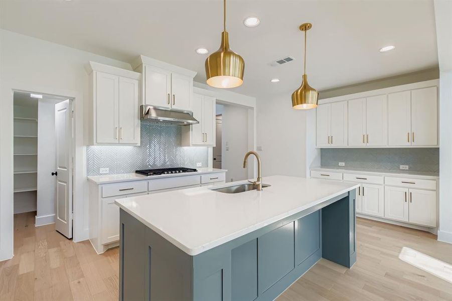Kitchen with backsplash, white cabinets, light wood finished floors, decorative light fixtures, and a center island with sink