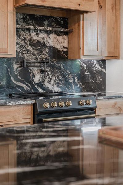 Kitchen featuring light wood finish cabinets, backsplash, electric range oven, and dark stone counters