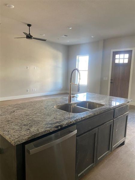 Kitchen with stainless steel dishwasher, stone counters, and sink