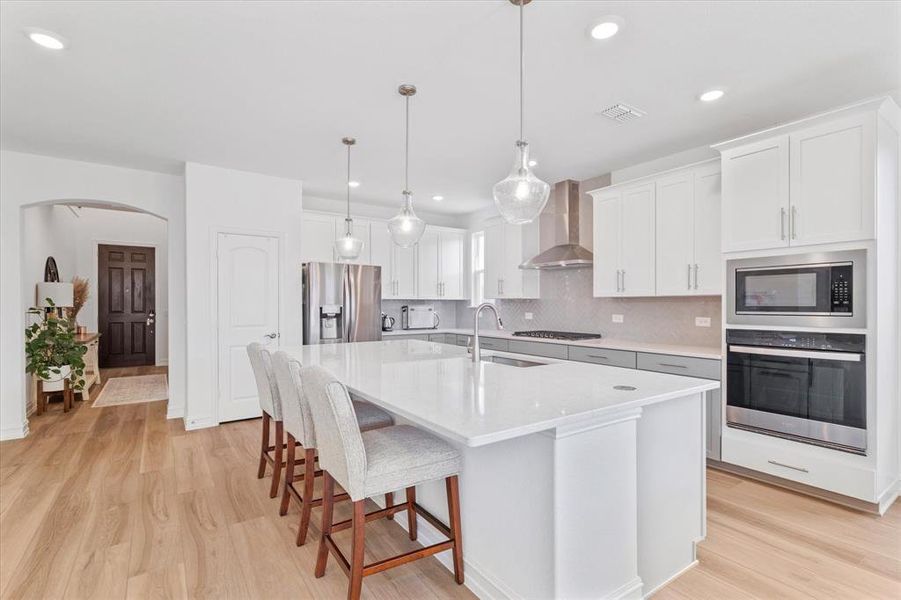 Kitchen featuring a large central island with seating, pendant lighting, stainless steel appliances, a tile backsplash, and wood-finish flooring