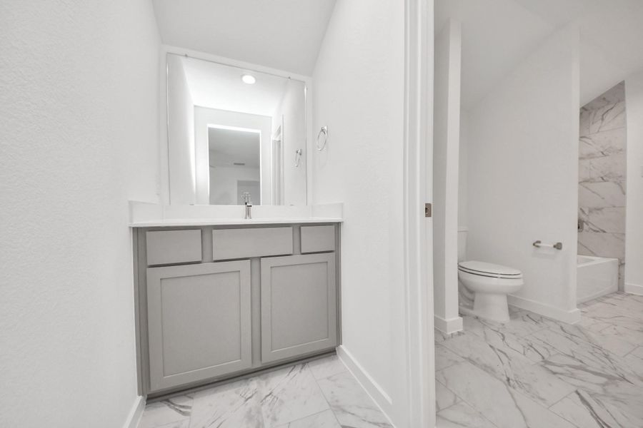 Experience convenience in the secondary bathroom, designed for Jack and Jill arrangements, now with a separate vanity area. This well-appointed space showcases stylish tile flooring, a bath/shower combo with an elegant tile surround, and light-stained wood cabinets. The beautiful light countertop adds a touch of sophistication, combining functionality and aesthetics seamlessly. Sample photo of completed home with similar floor plan. Actual colors and selections may vary.