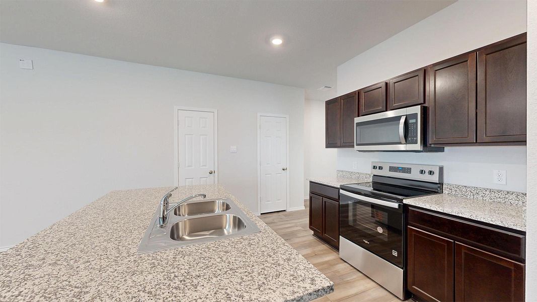 Kitchen featuring stainless steel appliances, a kitchen island with sink, dark wood finish cabinetry, light wood-style flooring, and recessed lighting