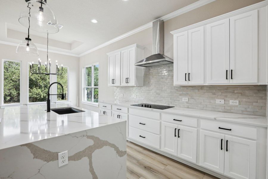 Kitchen with light stone counters, a raised ceiling, white cabinetry, pendant lighting, and ornamental molding