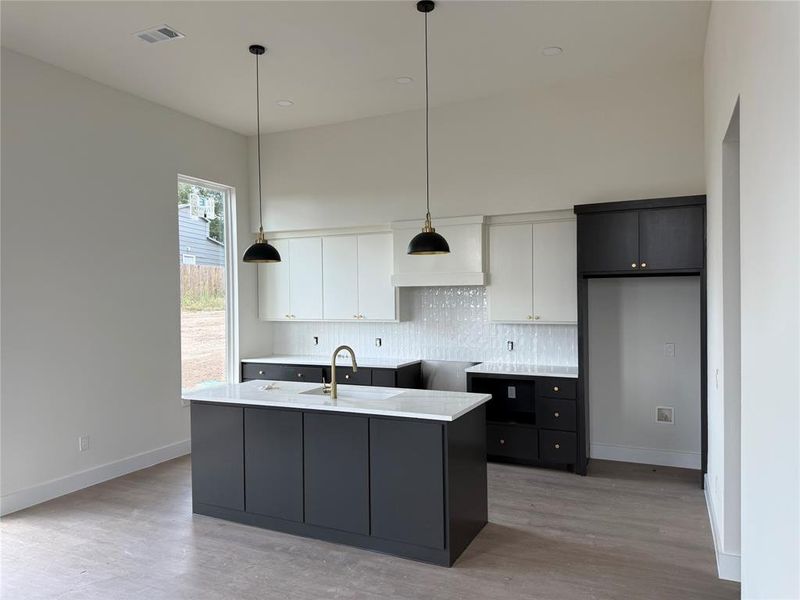 Kitchen with dark cabinetry, decorative light fixtures, white cabinets, decorative backsplash, and an island with sink