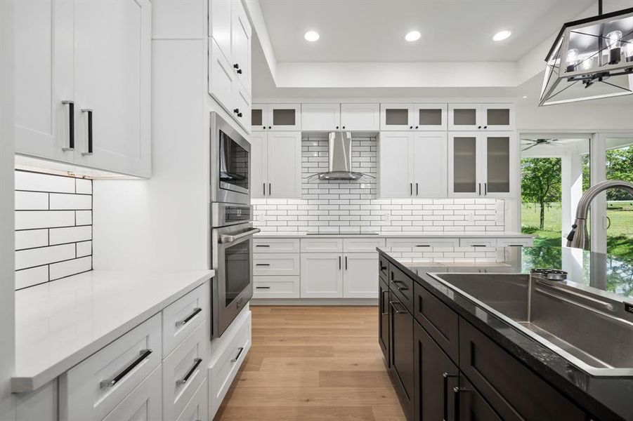 Two tone kitchen featuring light wood-type flooring, stainless steel appliances, light stone counters, and dual tone cabinets