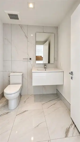 Floating vanity with a white integrated basin, floor-to-ceiling large-format tile wall, white stone-patterned floor tiling, rectangular mirror, and chrome single-handle faucet Floating vanity with a white integrated basin, floor-to-ceiling large-format tile wall, white stone-patterned floor tiling, rectangular mirror, and chrome single-handle faucet