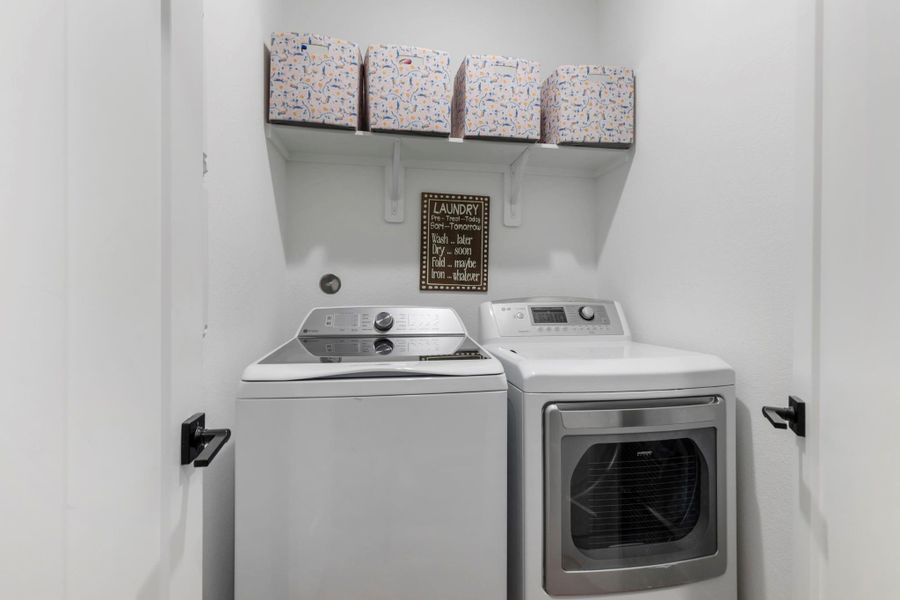 This photo shows a compact laundry room with a modern washer and dryer set. There's a small shelf above for storage, holding three decorative boxes. The space is clean and efficiently designed. This photo shows a compact laundry room with a modern washer and dryer set. There's a small shelf above for storage, holding three decorative boxes. The space is clean and efficiently designed.