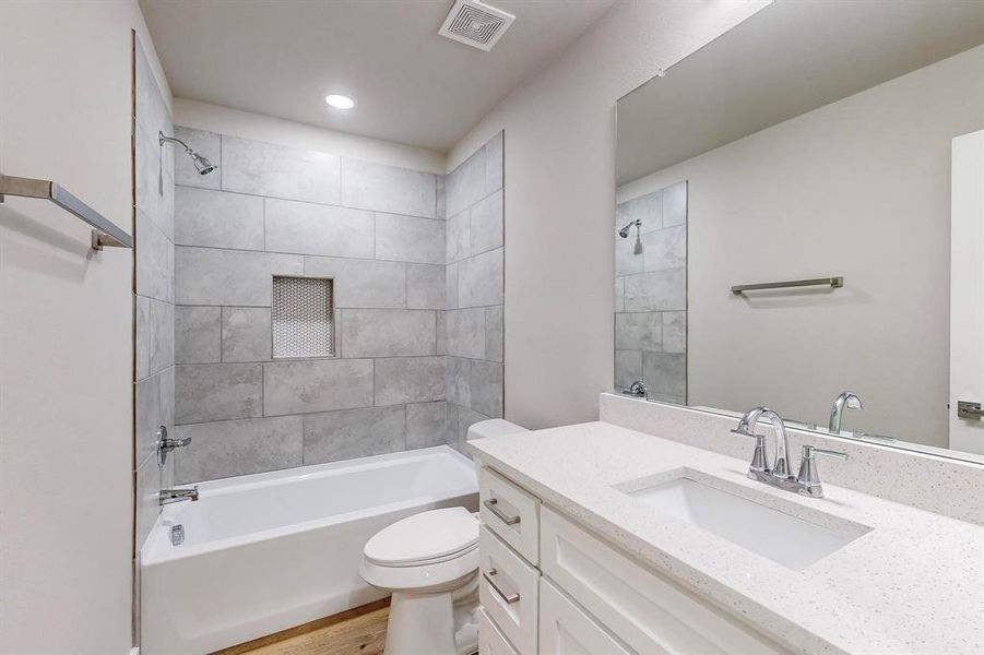 Full bathroom featuring hardwood / wood-style floors, tiled shower / bath combo, toilet, and vanity