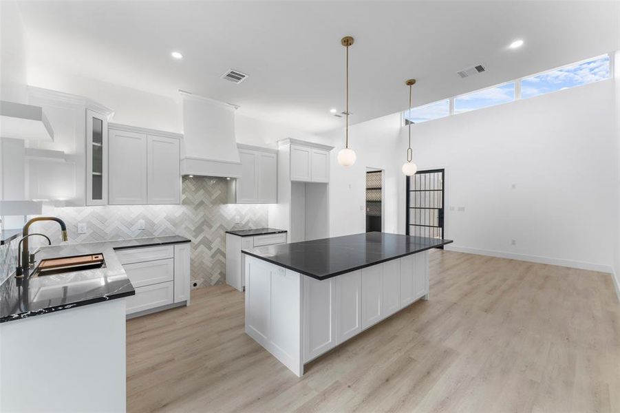Kitchen with tasteful backsplash, a center island, white cabinetry, decorative light fixtures, and light wood-style floors