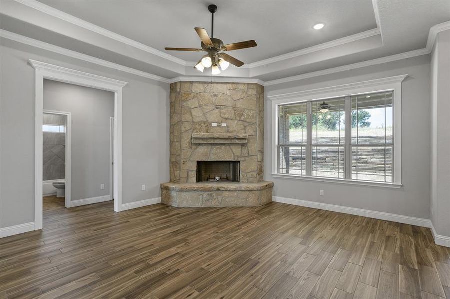 Unfurnished living room with crown molding, a raised ceiling, ceiling fan, a stone fireplace, and hardwood / wood-style flooring