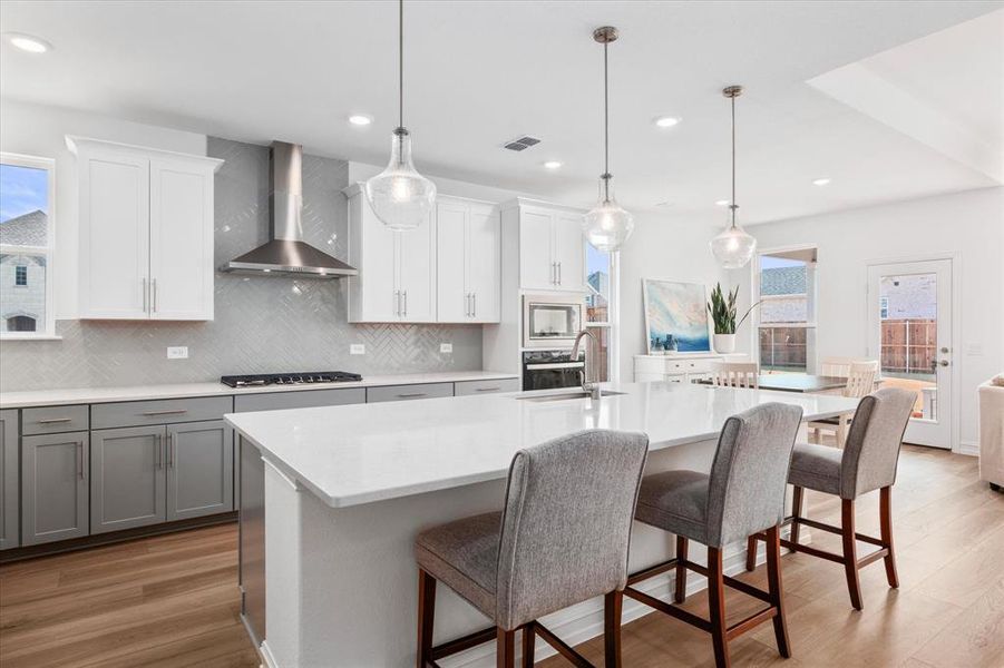 Kitchen with decorative backsplash, white cabinetry, wall chimney exhaust hood, light wood-type flooring, and decorative light fixtures