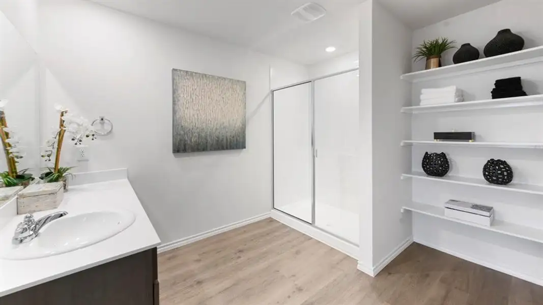 Bathroom featuring a single vanity with a white countertop and undermount sink, mirrored wall, wood-finish flooring, a glass-enclosed shower, and built-in shelving Bathroom featuring a single vanity with a white countertop and undermount sink, mirrored wall, wood-finish flooring, a glass-enclosed shower, and built-in shelving