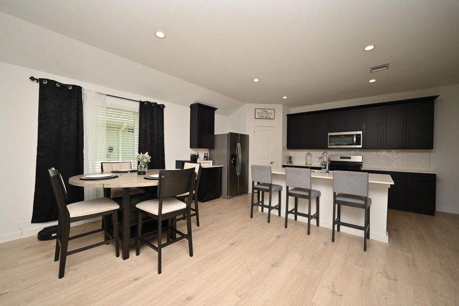 Modern kitchen and dining area with sleek black cabinetry, stainless steel appliances, and light flooring. The space features a center island with bar seating creating an inviting and functional open layout. Modern kitchen and dining area with sleek black cabinetry, stainless steel appliances, and light flooring. The space features a center island with bar seating creating an inviting and functional open layout.