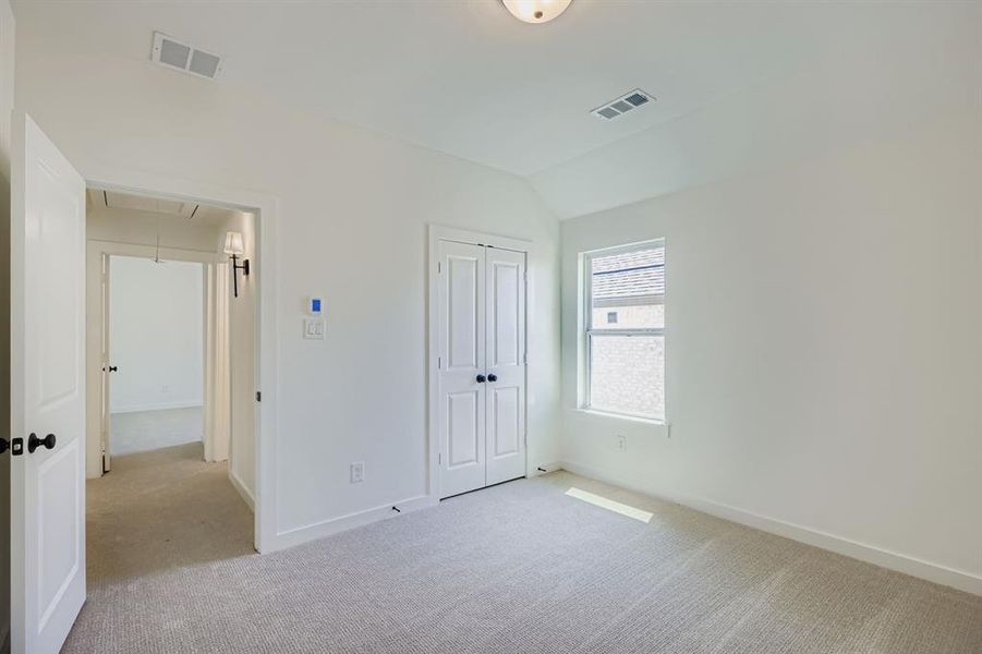 Unfurnished bedroom with attic access, light colored carpet, a closet, and vaulted ceiling