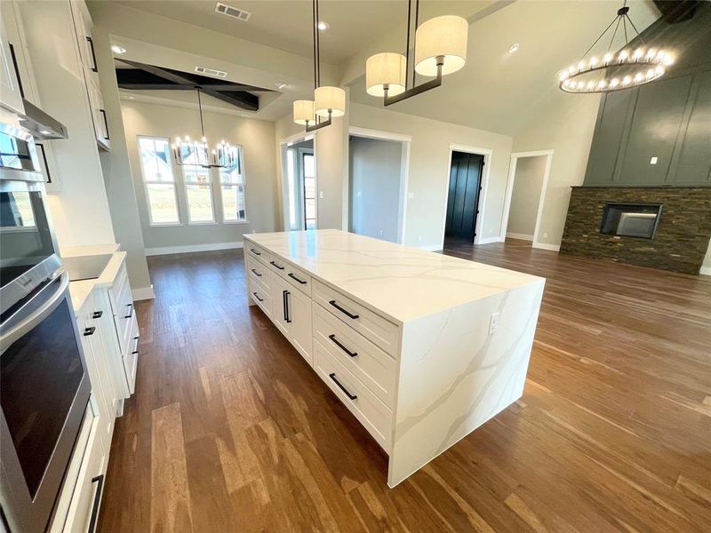 Kitchen featuring a center island, light stone counters, dark hardwood / wood-style flooring, pendant lighting, and white cabinets