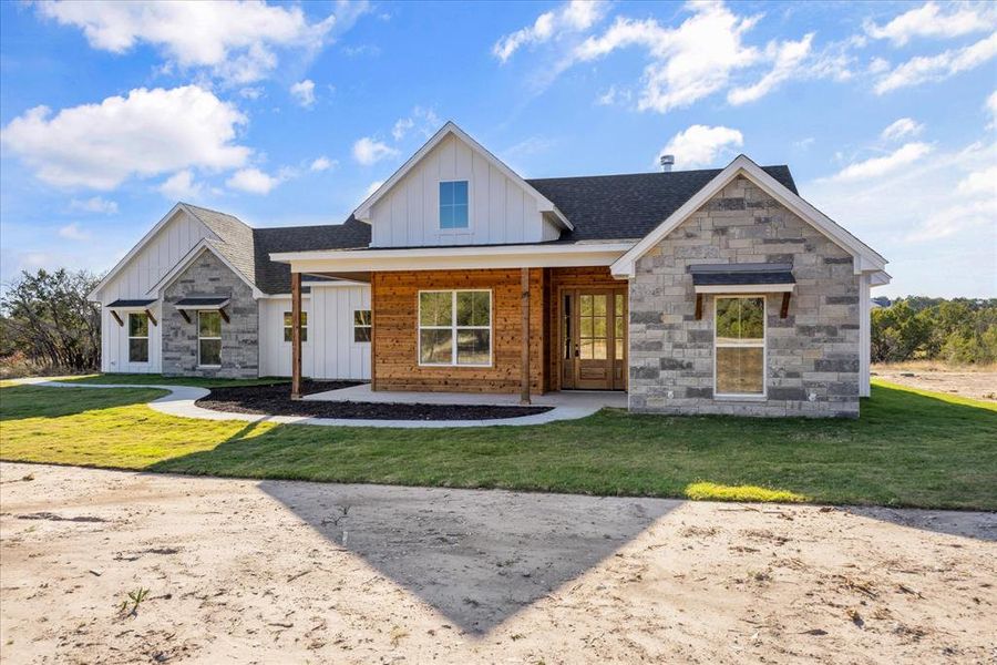 View of front of home with board and batten siding, a front yard, covered porch, and stone siding
