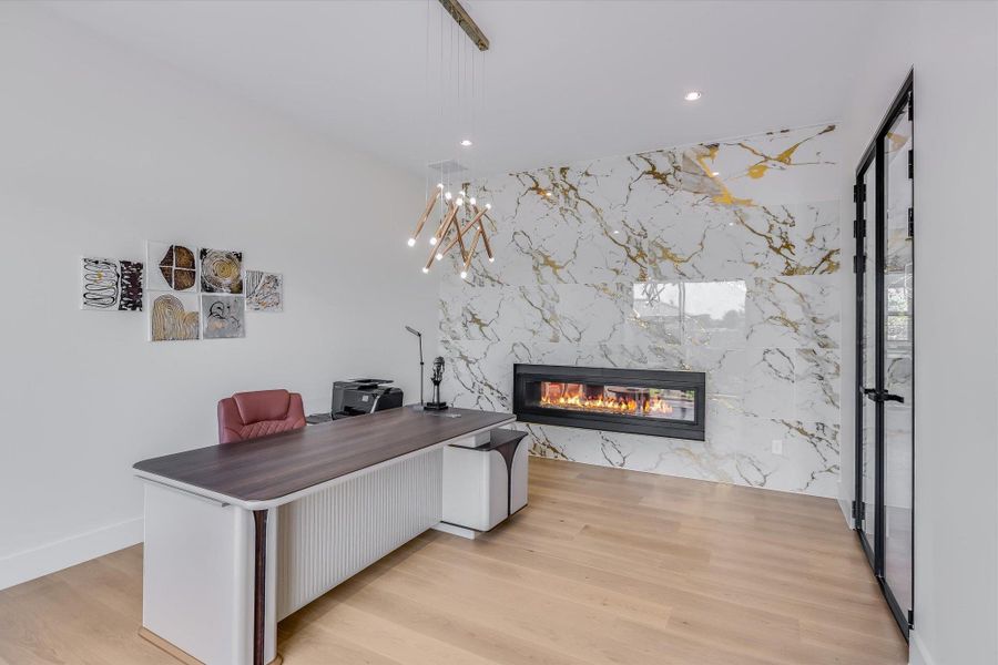 Office area featuring a marble fireplace wall, recessed and custom lighting, light wood finished floors, glass wall/door Office area featuring a marble fireplace wall, recessed and custom lighting, light wood finished floors, glass wall/door