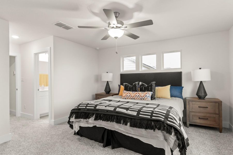 Well-lit sleeping quarters with a ceiling fan, plush carpeting, and direct access to an adjacent bath.