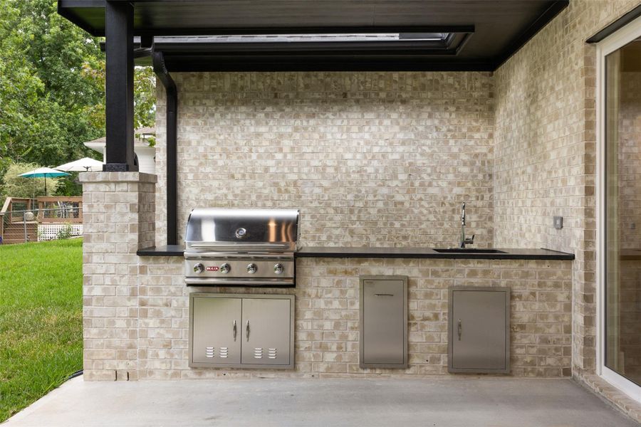Outdoor kitchen featuring built-in gas grill, sink, and granite countertops.