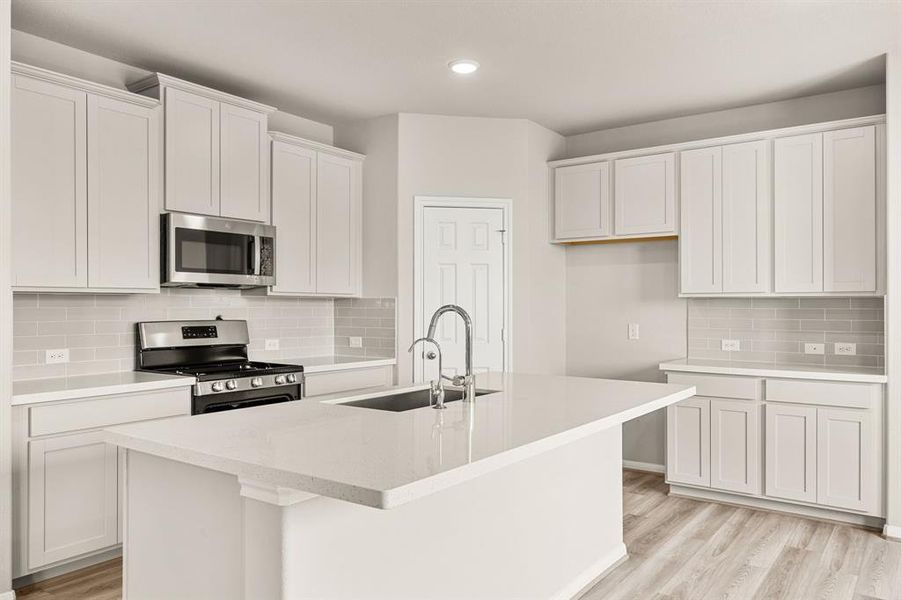 This light and bright kitchen features a large quartz island, white cabinets, a large sink overlooking your family room, recessed lighting, and beautiful backsplash.