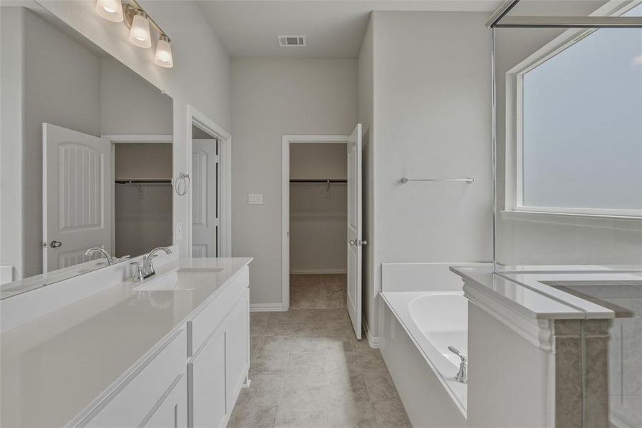 Bathroom featuring a double vanity with integrated sinks, a built-in soaking tub, a separate shower enclosure with a window, and a tile-finish floor Bathroom featuring a double vanity with integrated sinks, a built-in soaking tub, a separate shower enclosure with a window, and a tile-finish floor