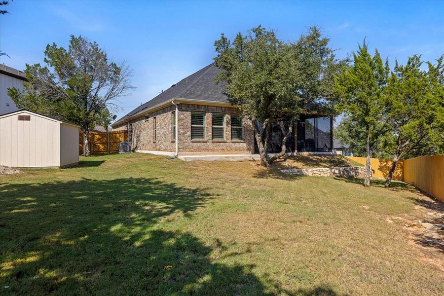 Back of house with a storage unit, a fenced backyard, brick siding, and a shingled roof Back of house with a storage unit, a fenced backyard, brick siding, and a shingled roof