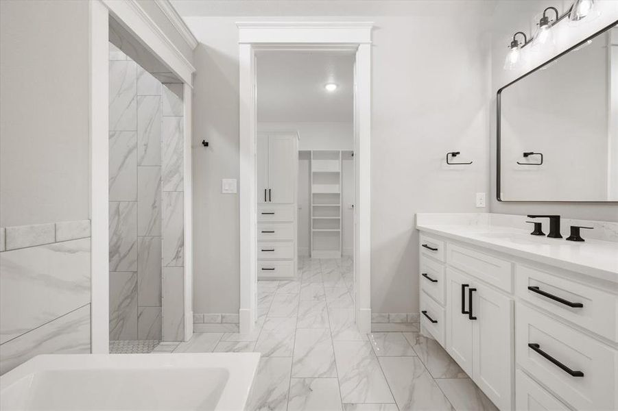 Spacious bathroom featuring a double vanity with white cabinetry and black hardware, a large rectangular mirror with black frame, and a tub with marble-look tile surround