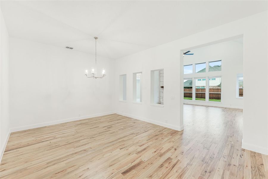 Empty dining and living area with light hardwood floors, chandelier, and large windows overlooking backyard