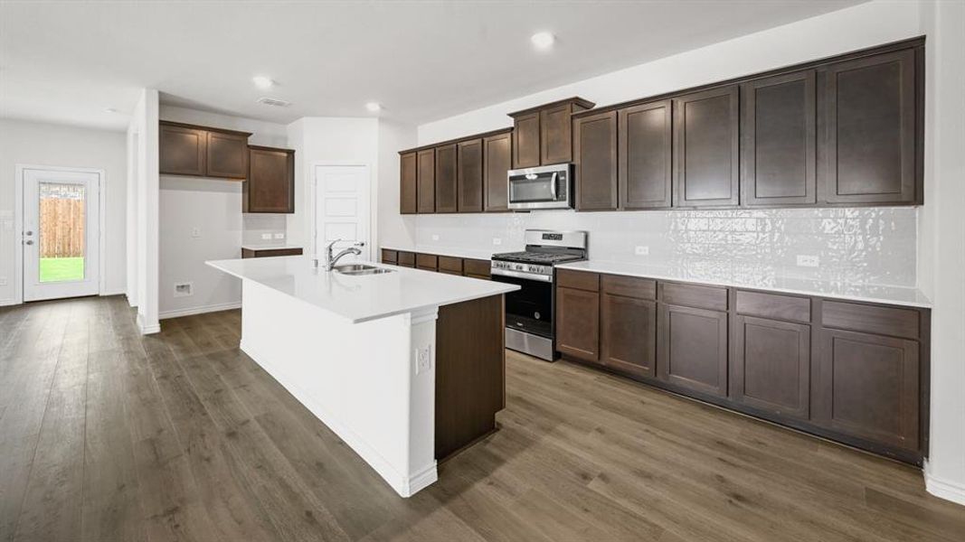 Kitchen featuring a spacious island, rich wood-finish cabinetry, bright white countertops, and a full suite of stainless steel appliances Kitchen featuring a spacious island, rich wood-finish cabinetry, bright white countertops, and a full suite of stainless steel appliances