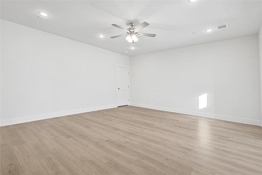This spacious room features light-toned wood flooring, a ceiling fan with integrated lighting, and recessed lighting for versatile illumination