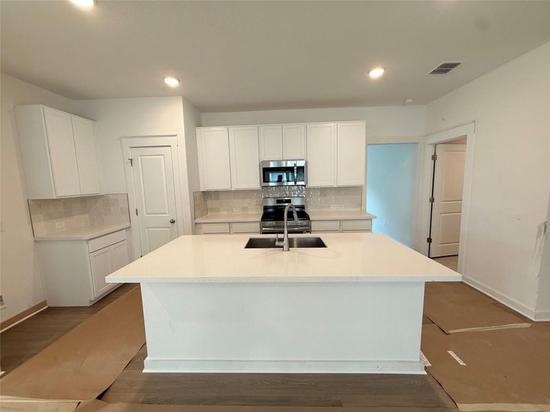 Kitchen with backsplash, an island with sink, white cabinetry, stainless steel appliances, and recessed lighting Kitchen with backsplash, an island with sink, white cabinetry, stainless steel appliances, and recessed lighting