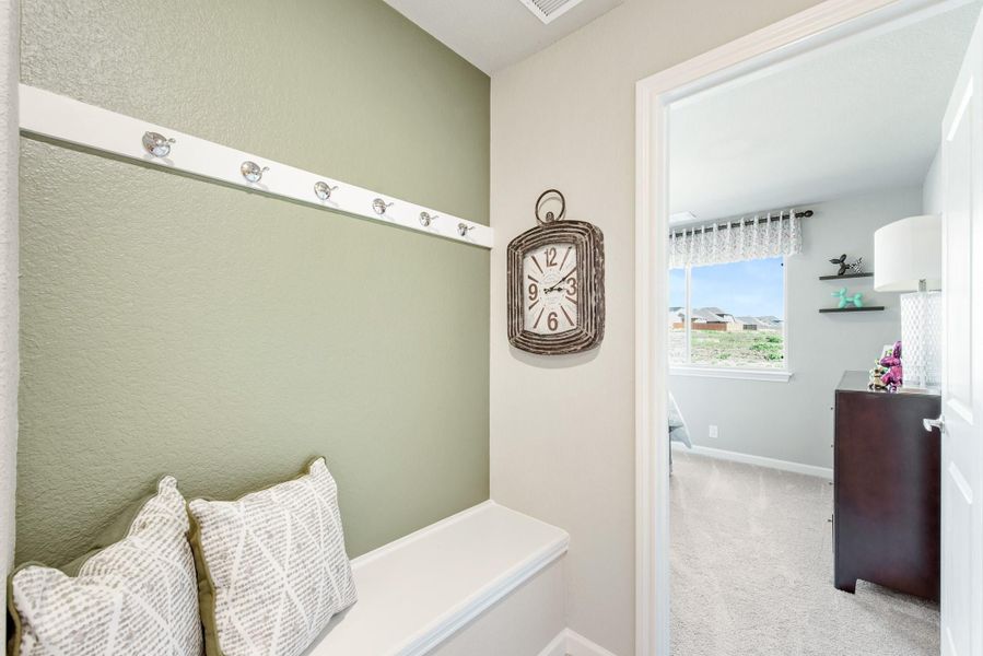 Mudroom nook with built-in bench, coat hooks, and green accent wall leading to carpeted bedroom Mudroom nook with built-in bench, coat hooks, and green accent wall leading to carpeted bedroom